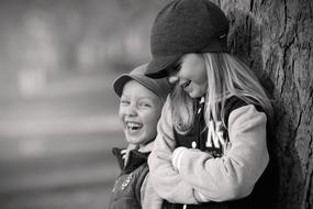 black and white portrait of a joyful boy and girl by the tree