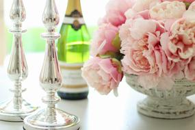 two candlesticks, a bottle of champagne and rouquettes of beautiful white and pink peonies in a vase on the table