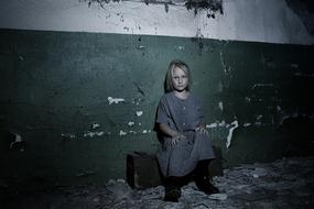 sad Child Girl sits at grunge wall in darkness