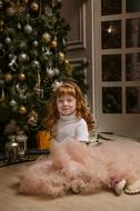 New Yearâs Eve, red haired child girl sits near christmas tree