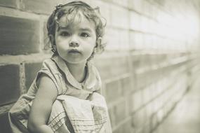 monochrome photo of a little girl by a brick wall