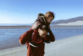 young happy Father with baby Son on shoulders on seaside