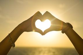 Beautiful heart shape of the hands, in colorful sunset, above the water