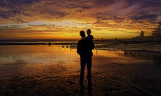 father with his son on the background of orange sunset