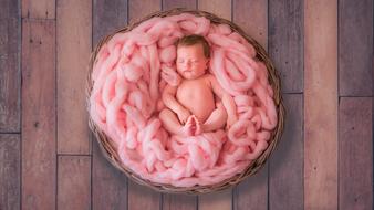 newborn among pink yarn in a basket on the wooden surface