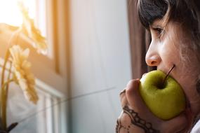 mature woman eating apple at window