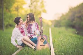 happy romantic couple in traditional clothes on the railroad among the plants