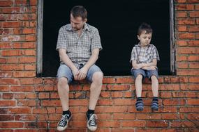 sad father and son are sitting on the windowsill of the brick building