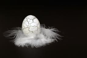 Glass Easter Egg and white feathers at black background