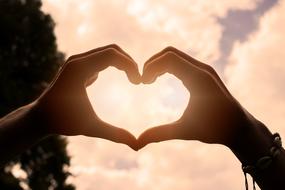 heart made of hands against the evening pink sky