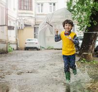 boy with umbrella runs through the puddles