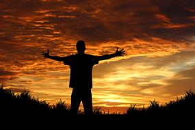 male silhouette with wide open arms at hot colored sunset sky