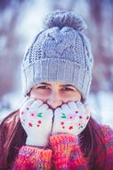 a girl in winter clothes presses her hands to her face