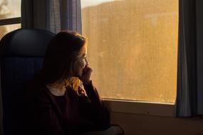 girl is looking out the window in a train