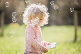 Nice child girl plays with soap bubbles outdoor