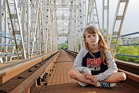 serious teen girl sits on railway bridge