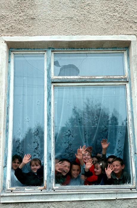 Children, smiling and waving hands, behind the window of the school in Moldova