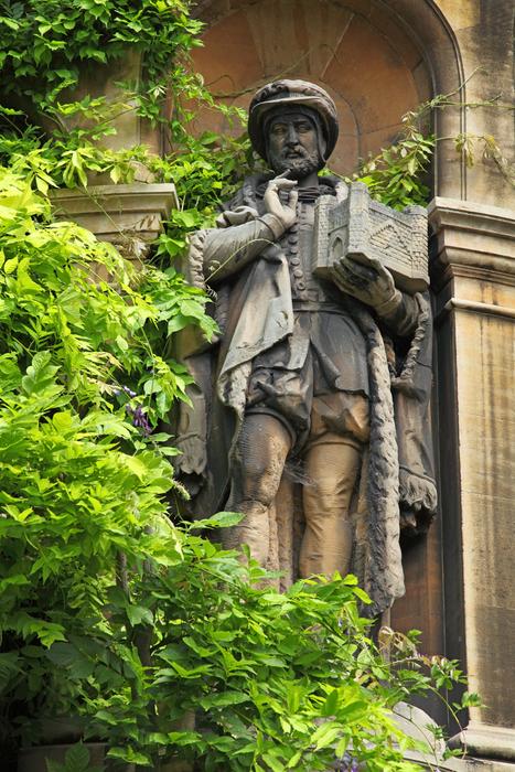 Beautiful statue of the man near the green trees near the campus of Cambridge in England