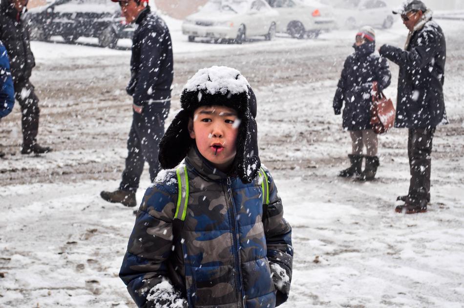 a schoolboy stands under a snowfall in Mongolia