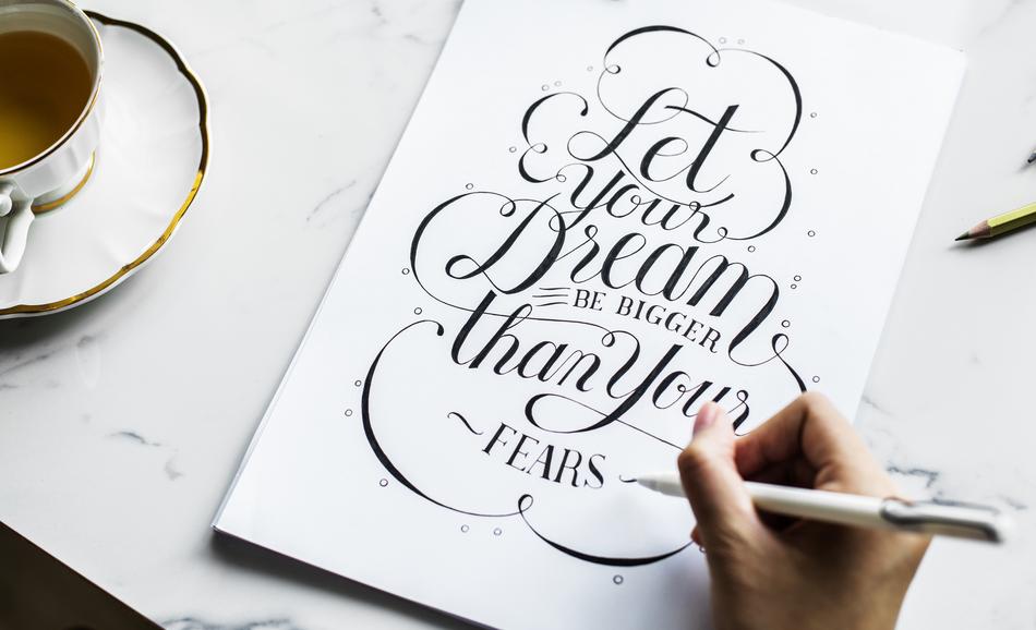 Artist, writing beautiful, black text on the white card, with the pen, near the cup of coffee