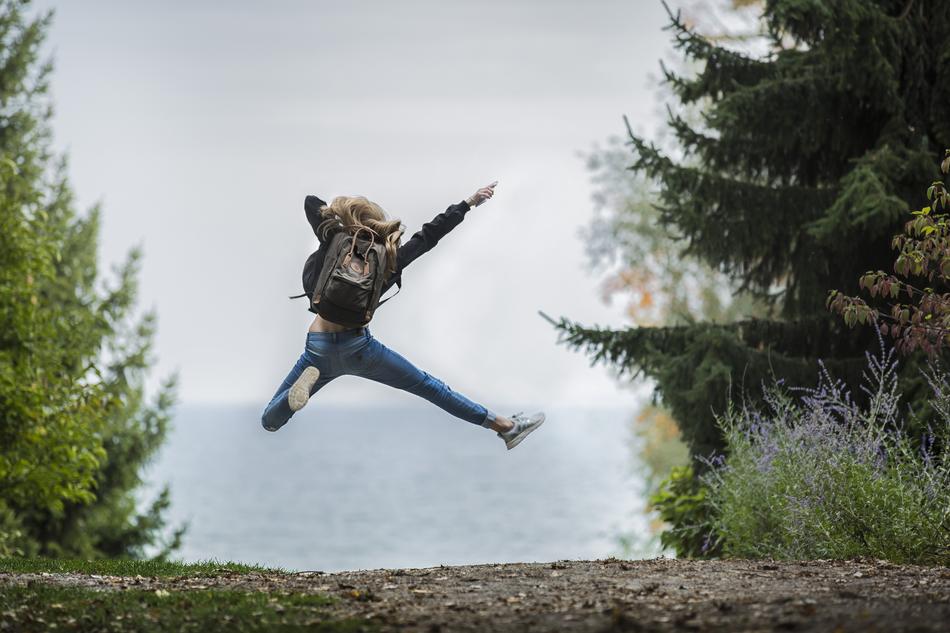 sportive girl with backpack jumps on path at water