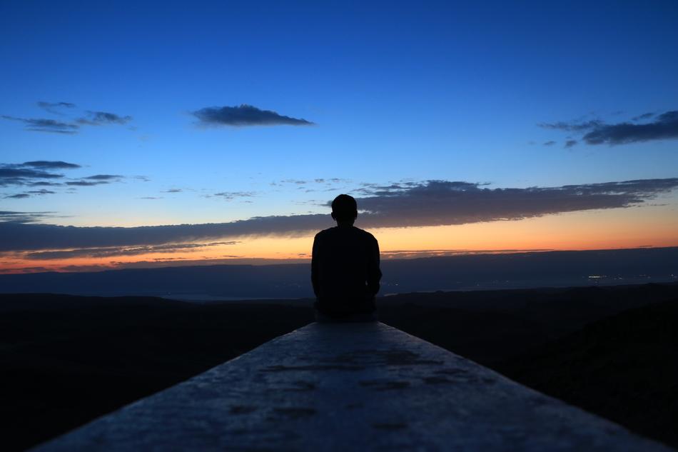 evening photo of a man sitting on a concrete fence