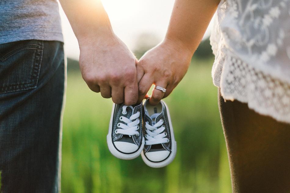 Couple, holding cute baby shoes in the hands, among the green and yellow plants