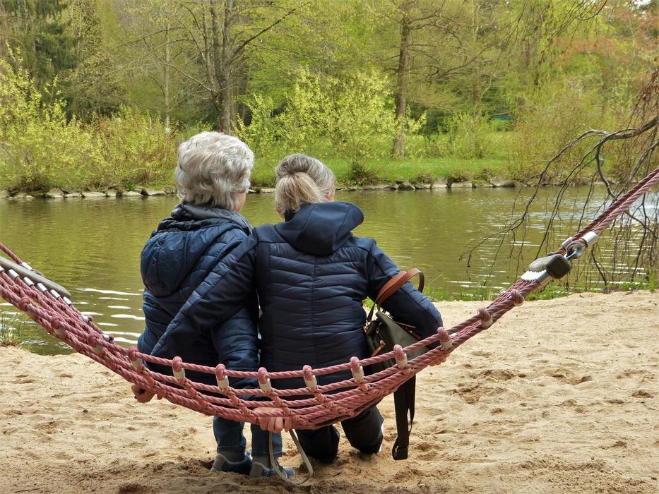 mom and daughter are sitting in a hammock on the lake