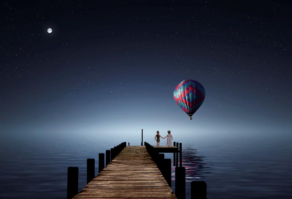 Fantastic image of a couple in love on the pier and hot air balloon against the night sky