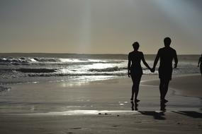 man and woman walking away holding hands on Beach at Sunset