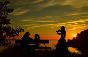 landscape of the female Silhouettes on a lake coast at Sunset