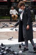 happy young girl feeding pigeons in city