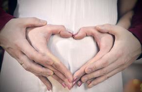 male and female hands in heart shape on pregnant belly, family love