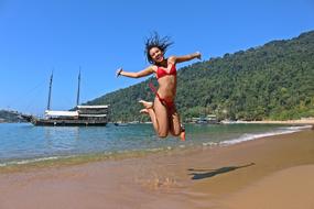 happy girl in red bikini jumps on the beach