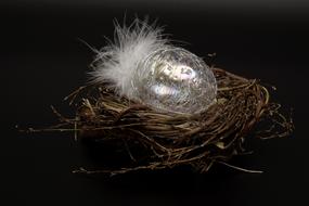Glass Easter Egg and white feather in nest in a dark