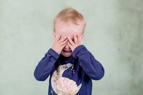 little boy covers his face with his hands