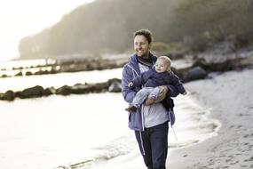 dad carries son in his arms along the coast