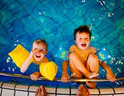 Smiling children, swimming in the pool, near the adult