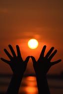 Silhouettes of the hands, on the beach, at colorful and beautiful sunset on background