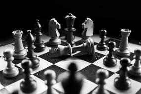 Black and white photo with the shiny chess pieces on the board, among the darkness