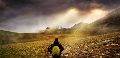 Man with yellow backpack walking among the colorful mountains