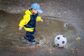 little boy with soccer ball in a puddle