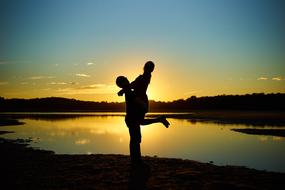 Silhouette of the couple, hugging on the beautiful shore of the lake, at colorful and beautiful sunset in the sky