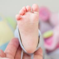 Close-up of the cute foot of the baby, in the parent's hand, at blurred background