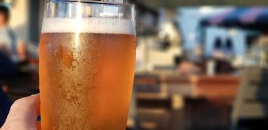 Wet glass of the beer, with foam, in the hand