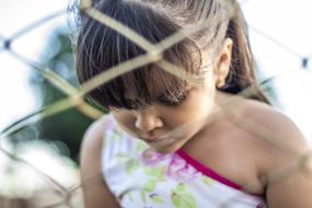little sad girl behind a wire fence in a blurred background