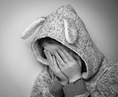 Black and white photo of a person in bunny hood, covering face with hands
