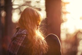 Beautiful, blonde girl, sitting in the colorful sunset, among the trees