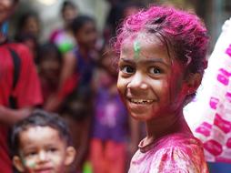 Portrait of the smiling child girl in colorful paint, among the other people