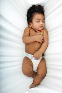Portrait of the cute baby with colorful toy, sleeping on the white bed